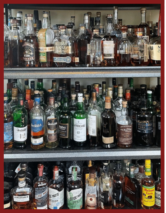 Three shelves filled with a wide variety of liquor bottles, including whiskey, rum, and other spirits, showcasing a well-stocked collection.