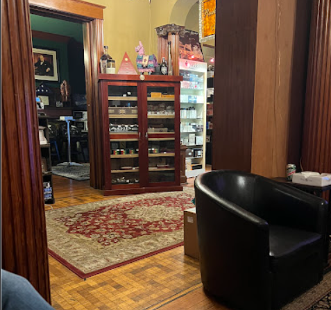 A well-appointed room featuring a dark leather armchair, an ornate red and cream rug on a hardwood floor, and a large wooden cabinet displaying various items in the background.